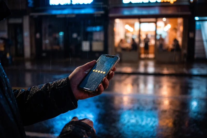 Hand holding a phone showing five stars on a rainy street at night